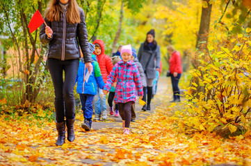 teacher leads a group of children for a walk in the autumn park, holding hands and walking along the path, playing outdoors