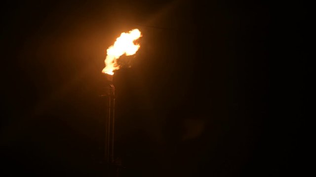 A night shot of a flaming gas torch of petrochemical production in complete darkness. Low key oil combustion and environmental pollution. Ecology problems concept