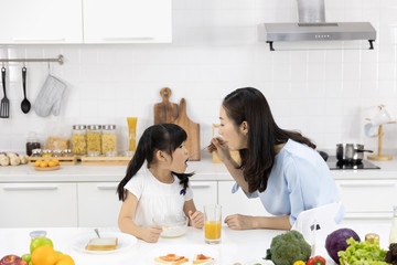 Happy Asian family Mother and Little girl are eating breakfast, cereal  with milk in the kitchen at home. Healthy food concept For the strength of the body