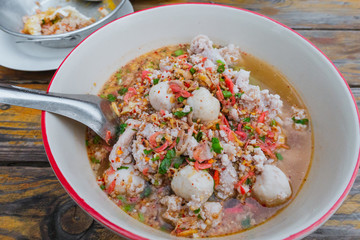 Traditional Thai food noodle soup tom yam with Pork Chops, meat ball, Red pork in big bowl on wooden table background.