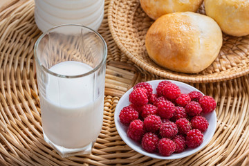 red raspberries on a white saucer, milk and fresh homemade buns for a delicious breakfast