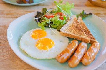 American breakfast set with bread , fried eggs grill sausage and vegetable salad on blue dish on wooden table background with copy space in morning.