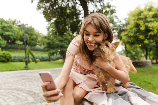 Portrait of happy caucasian woman taking selfie photo with smartphone while sitting on bench in summer park