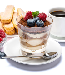 Classic tiramisu dessert with blueberries and raspberries in a glass cup, savoiardi cookies and espresso coffee on white background with clipping path