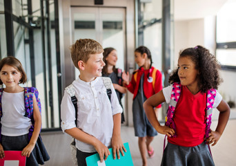 A group of cheerful small school kids with bags walking in corridor.