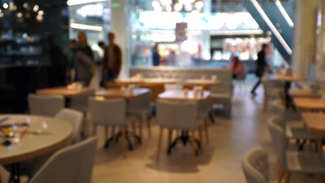 Abstract bokeh background of blurred coffee house in mall with people and waiters. Visitors come to premises of small restaurant for lunch.