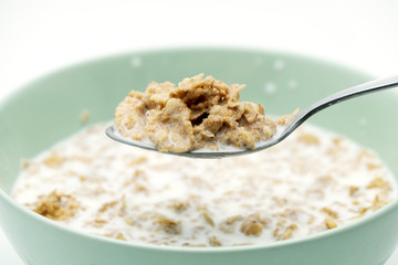 Scoop of the cereal flake with milk by stainless steel spoon from the green bowl isolated on white background
