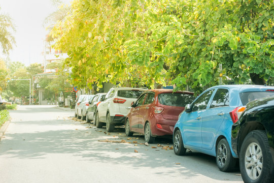 Parallel cars parking on street with green trees