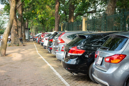 Parallel cars parking on street with green trees