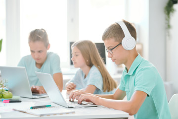 Fototapeta premium One of youthful classmates in headphones looking at laptop display