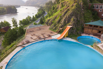 outdoor pool in the Altai mountains with a yellow water slide attraction with wooden chaise-longue,...