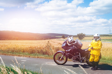Fototapeta na wymiar The driver girl in helmet is wearing a raincoat. Adventure motorbike with bags. a motorcycle tour journey. Outdoor. light warm tinting, glow, freedom concept. field and sky on background, copy space
