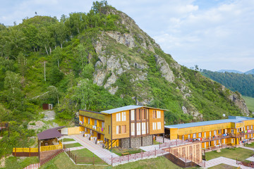 Aerial view of wooden houses and hotels in the mountains among the rocks and green trees for relaxation and accommodation during tourist trips and travel with parking in the courtyard on a summer day.