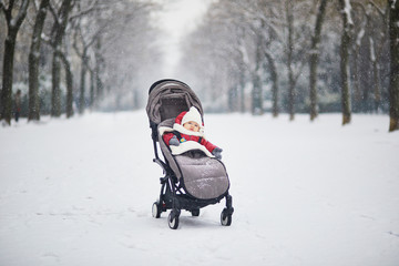 Fototapeta na wymiar Happy smiling baby girl in stroller in Paris day with heavy snow