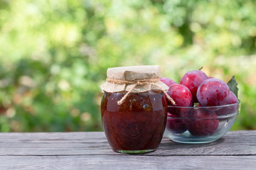 Jar of plum jam with plums on wooden table