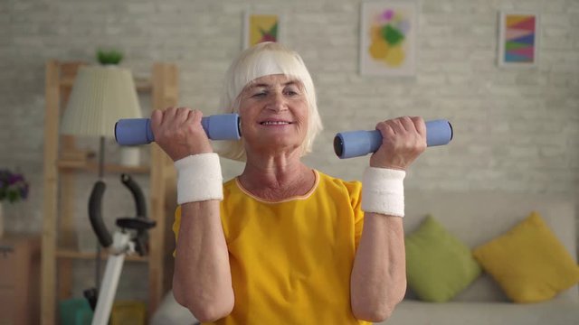 Active sports fitness granny engaged in charging with dumbbells in the living room close up