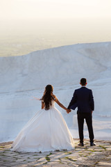 Young wedding couple stands over cliff holding hands and looks into the distance