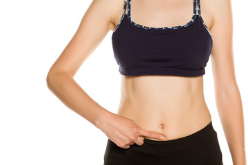 Fototapeta na wymiar Young sporty woman pointing finger at her belly, tummy. Isolated on white background. Closeup.
