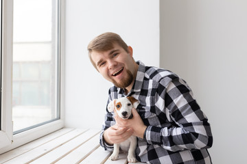 people, pets and animals concept - young man hugging jack russell terrier puppy