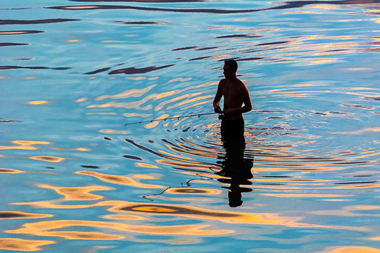 silhouette of a fisherman in reflection in water ripples