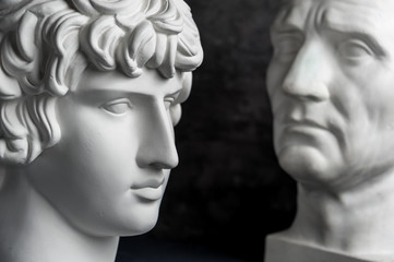 Gypsum copy of ancient statue Augustus and Antinous head on dark textured background. Plaster...