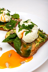 Poached eggs with avocado, spinach leaves and seeds on toasts bread on a white plate on the white background. Healthy breakfast or snack. Close-up.