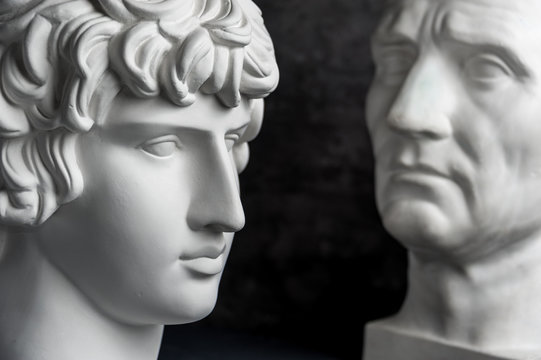 Gypsum copy of ancient statue Augustus and Antinous head on dark textured background. Plaster sculpture mans face.