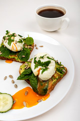 Poached eggs with avocado, spinach leaves and seeds on toasts bread on a white plate on the white background. Healthy breakfast or snack.