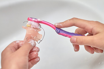 A girl brushes a removable orthodontic appliance. Concept of pediatric dentistry, correcting the bite. Closeup, selective focus