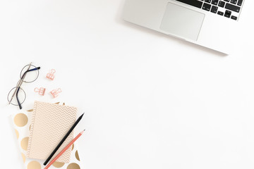 Workspace on white desk with laptop, notepads, glasses and stationery