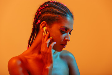 Amazing pretty young african naked woman posing isolated over yellow neon lights wall background...