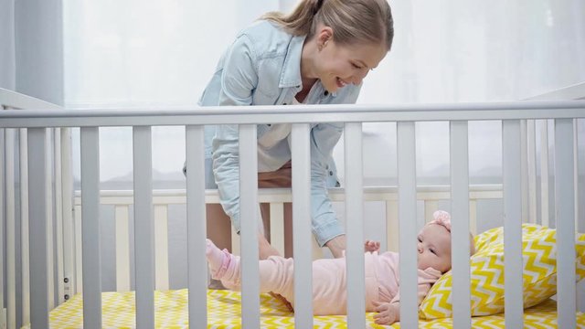 happy mother putting infant in baby crib 
