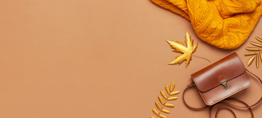 Brown leather women bag, orange knitted sweater, golden autumn leaf on brown background top view flat lay copy space. Fashionable women's accessories. Autumn Fashion Concept. Stylish Lady Clothes