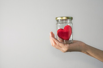Female holding red heart in glass bowl.
