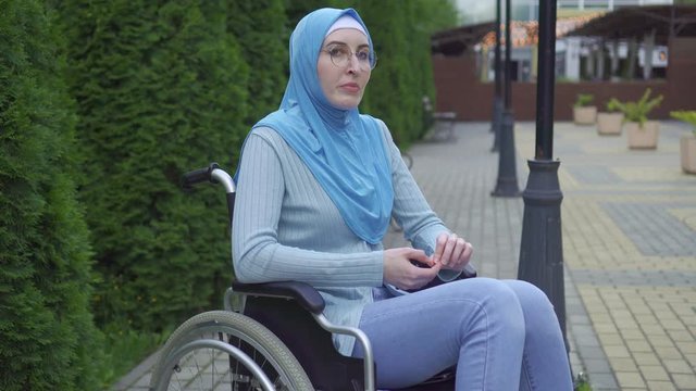 Portrait lonely sad young muslim woman disabled in a traditional scarf sitting in a wheelchair in the park