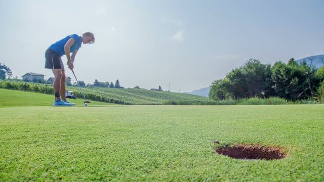 A woman is playing golf on the golf course. She concentrates before hitting a golf ball gently. However, it doesn't fall into a hole. A woman misses it.