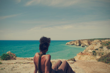 Black woman looking at the sea sitting on a cliff in Algarve, Portugal