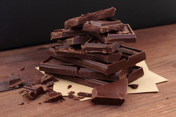 heap of broken pieces of dark bitter chocolate. Slices of chocolate bar and crumbs. Sweet dessert on homemade paper on a wooden table. ready to eat concept, dark background