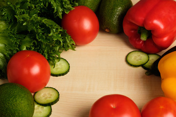 Vegetables are lying on a light wooden table with empty space in the middle.