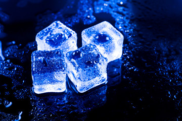 Blue ice cubes on black wet table.