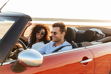 Beautiful young multiethnic couple riding in a convertible - obrazy, fototapety, plakaty