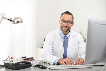 portrait of a handsome man male doctor in medical practice office working on computer