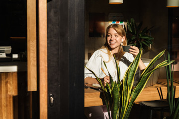 Portrait of beautiful young woman smiling while drinking coffee and using laptop computer in cafe