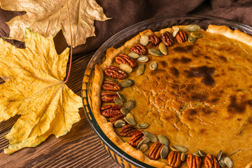 Homemade traditional pumpkin pie decorated with nuts and seeds. Natural rustic style wooden background. Selective focus.