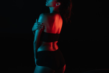 cropped view of red lighting on young woman in underwear standing isolated on black