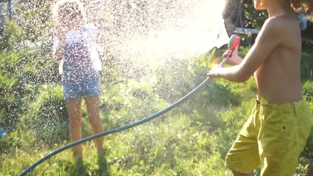 Little boy is pouring a water from a hose at his sister. Brother and sister happy children in summer heat water each other with water, summer vacation