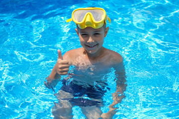 Naklejka premium A child in a mask for swimming. A young boy in the pool shows thumbs up. Kid are engaged in diving.