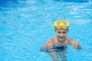 A child in a mask for swimming. A young boy in the pool shows thumbs up. Kid are engaged in diving.