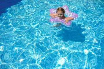 A little girl is swimming in the outdoor pool. The child is floats in an inflatable circle.