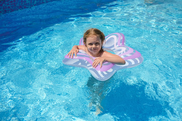 Fototapeta na wymiar A little girl is swimming in the outdoor pool. The child is floats in an inflatable circle.